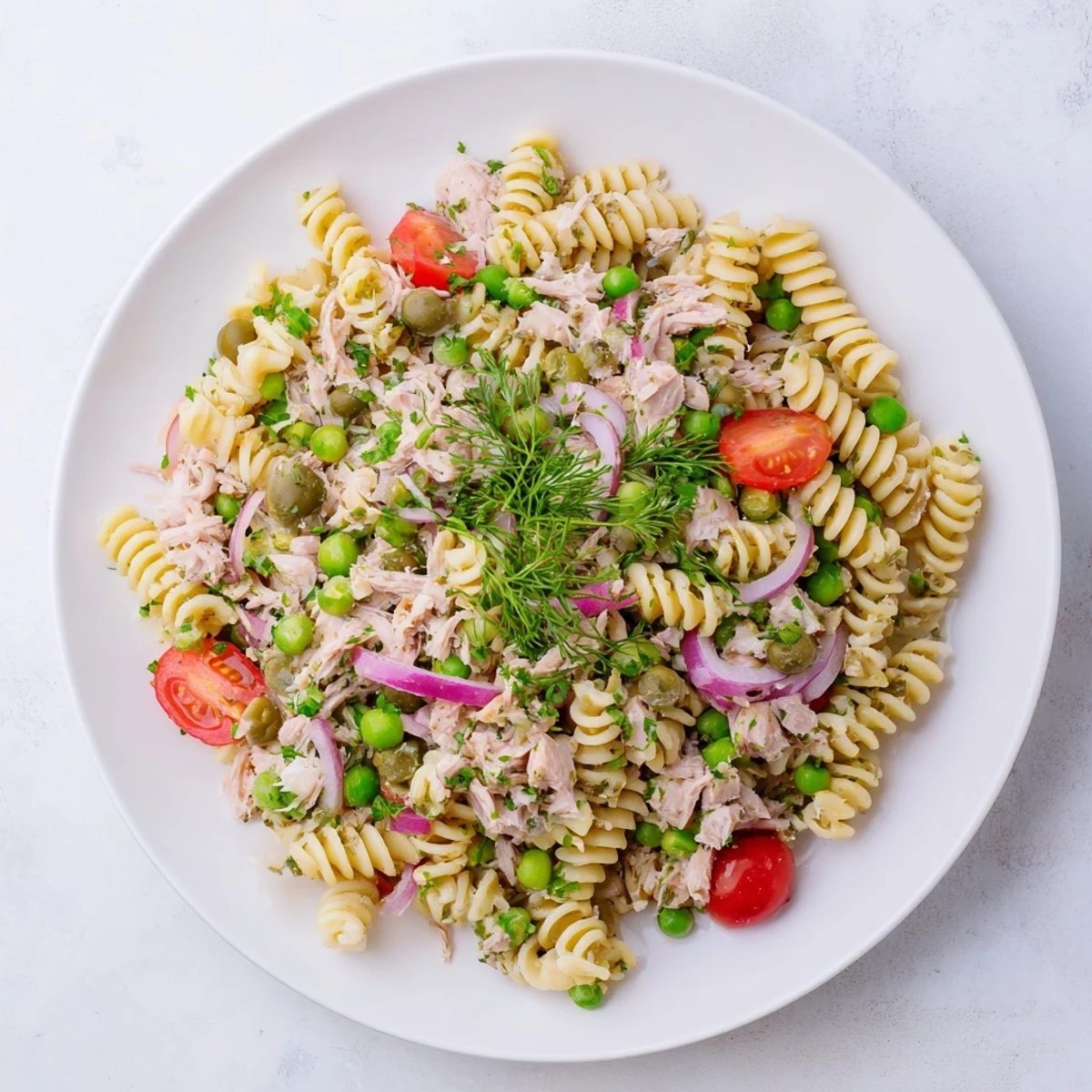 Ein leckeres Lemony Tuna Pasta Salad auf einem weißen Teller, garniert mit frischen Kräutern und Zitronenscheiben.