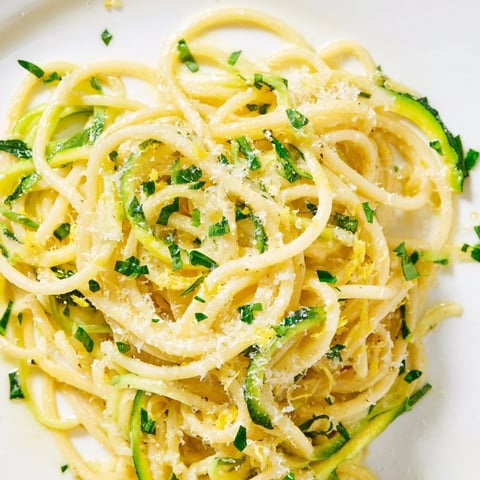 Gebettelte Zucchini-Nudeln in einer cremigen Zitronenbutter-Sauce, garniert mit frischem Petersilienkäse, serviert auf einem hellem Tellerteller.