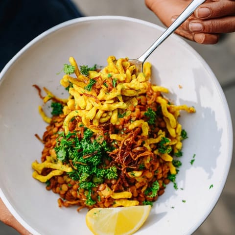 A steaming bowl of vegan German Dahl & Spätzle, garnished with crispy onions and fresh herbs.