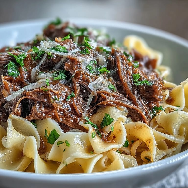 Langsam gegartes Rindfleisch in würziger Brühe mit Zwiebeln auf Butter-Eiernudeln angerichtet