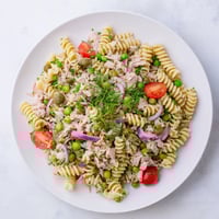 Ein leckeres Lemony Tuna Pasta Salad auf einem weißen Teller, garniert mit frischen Kräutern und Zitronenscheiben.