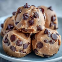 Zu 100 % pflanzliche Vegan Chickpea Cookie Dough Bites mit dunklen Schokoladenstückchen auf einer rustikalen Holzplatte
