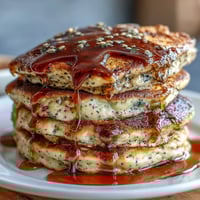 Fluffige schwarze Sesam-Pfannkuchen mit nussigem Aroma und goldener Kruste, serviert mit Ahornsirup.  