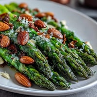 Zitronenbutter-Asparag mit Mandeln auf einem weißen Teller, mit goldenen Mandeln bestreut und einem Hauch Zitronenschale.